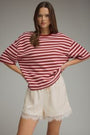 Woman wearing a red and white striped shirt and beige shorts on a gray background