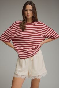 Woman wearing a red and white striped shirt and beige shorts on a gray background