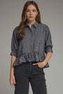 Woman wearing a navy checkered blouse with ruffled bottom and black pants on a gray background