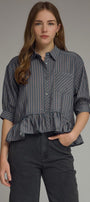 Woman wearing a navy checkered blouse with ruffled bottom and black pants on a gray background
