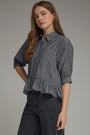 Woman wearing a gray striped shirt with a ruffled bottom on a plain background