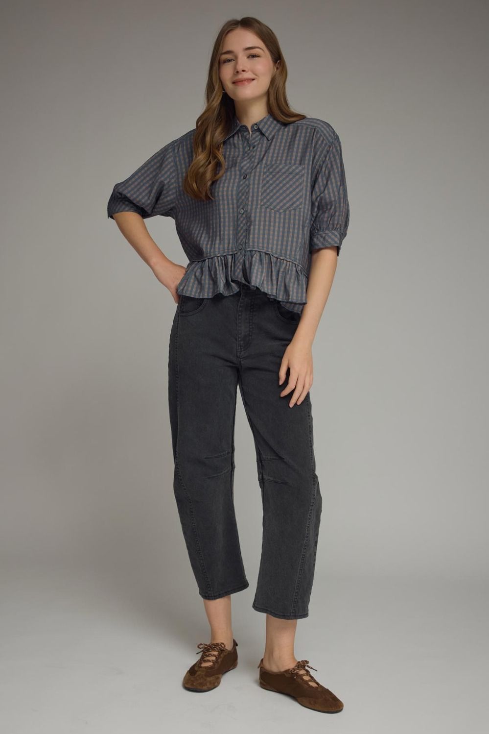 Woman wearing a navy checked shirt and dark pants on a plain background