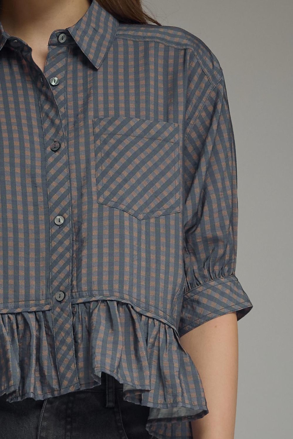 Checkered shirt with ruffled bottom worn by a person on a gray background