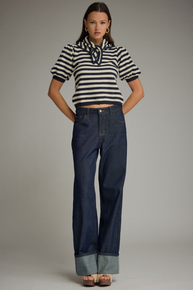 Woman wearing a striped shirt and blue jeans against a plain background