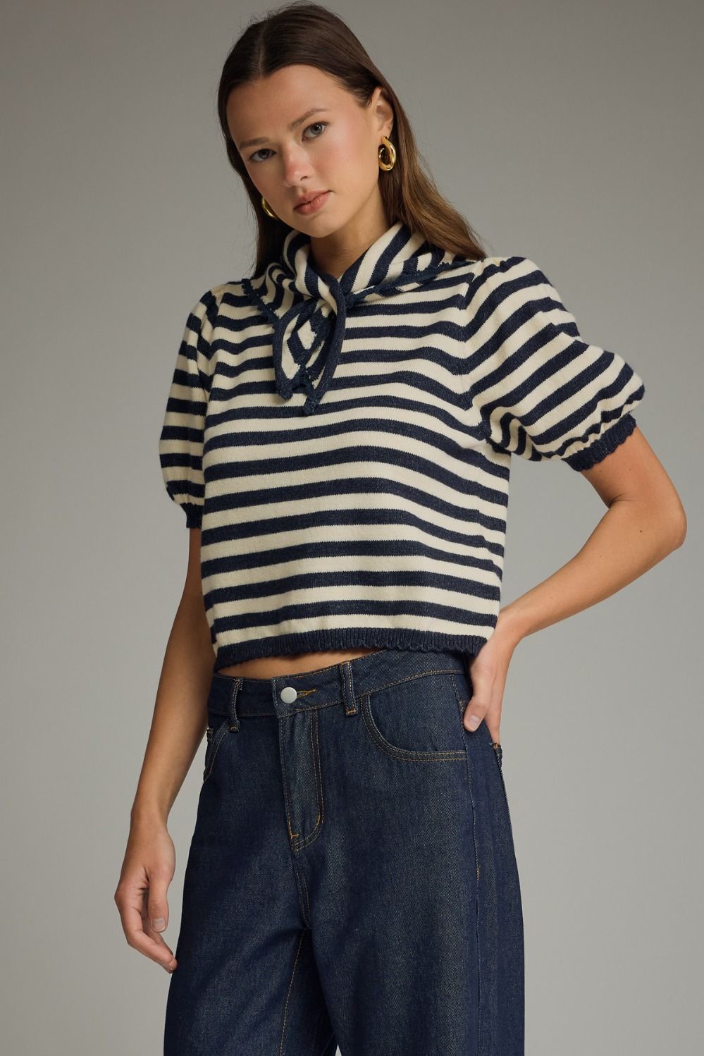 Woman wearing a striped sweater and jeans against a gray background