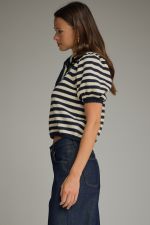 Woman wearing a striped shirt and dark pants against a plain background