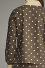 A close-up back view of a brown long-sleeve top with a cream polka dot pattern, shown on a mannequin against a neutral gray background.