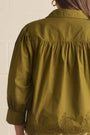 An olive green long-sleeve blouse with a gathered, smocked bodice and delicate lace embroidery along the hem, shown from the back.