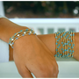 Arm wearing multiple gold and turquoise beaded bracelets with a blurred background