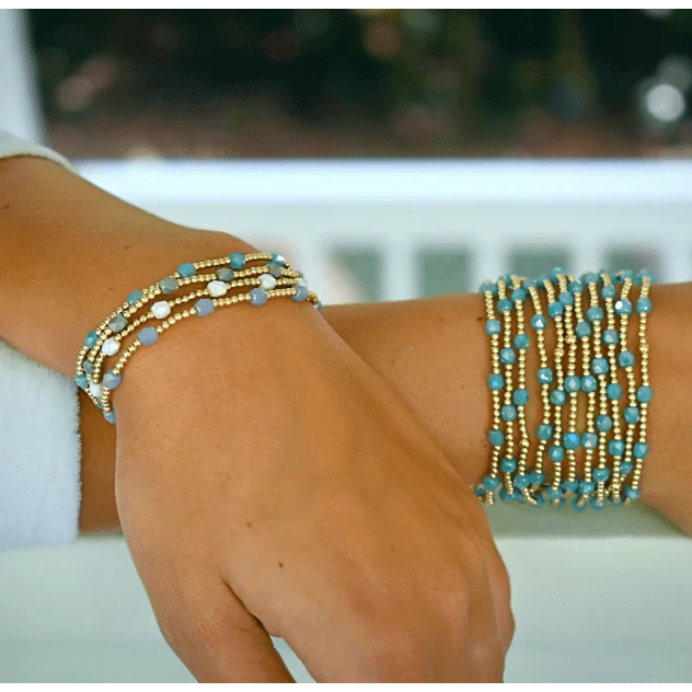 Arm wearing multiple gold and turquoise beaded bracelets with a blurred background