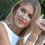Woman with blonde hair and pink lipstick wearing multiple gold bracelets and rings.