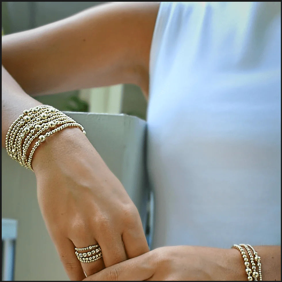 Close-up of a hand wearing gold bracelets and a ring, with a blurred background.
