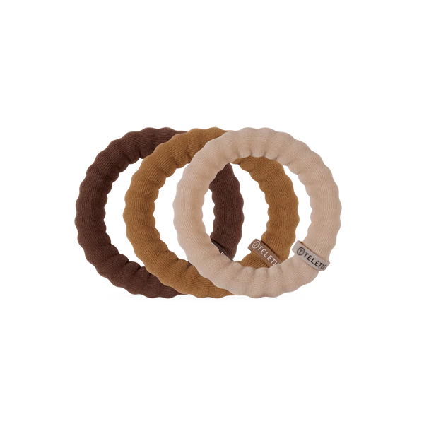 Three ribbed fabric hair ties in dark brown, tan, and light beige, overlapping on a plain white background. Each tie has a small fabric tag with the brand name TELEF.