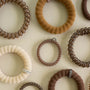 An assortment of fabric and elastic hair ties in various colors and textures, including brown, beige, and cream, arranged on a light cream background.