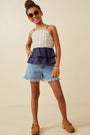 Young girl wearing a layered top and denim shorts with sunglasses on a beige background