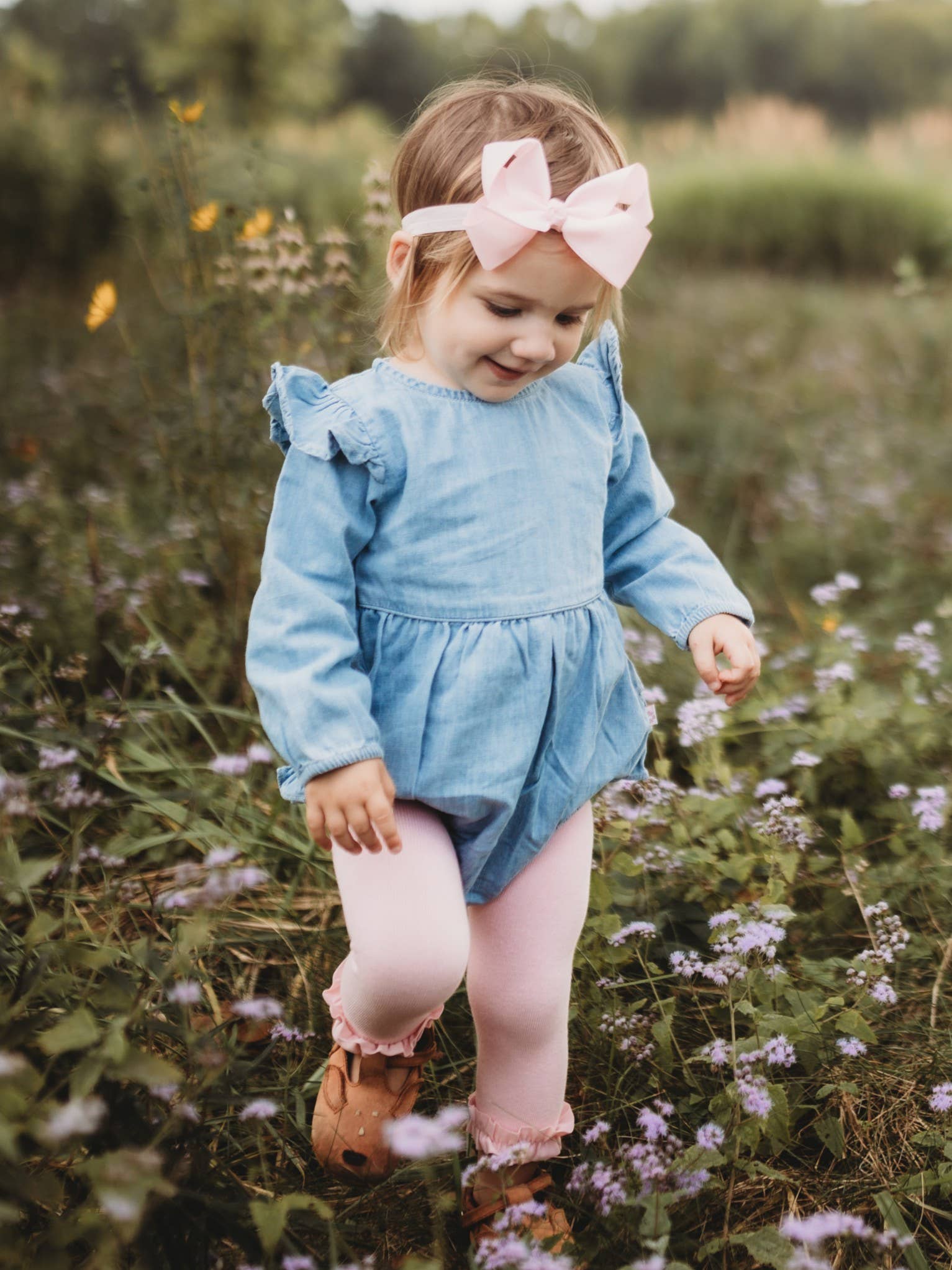 Young girl in a blue dress with a large pink bow standing in a field of flowers.