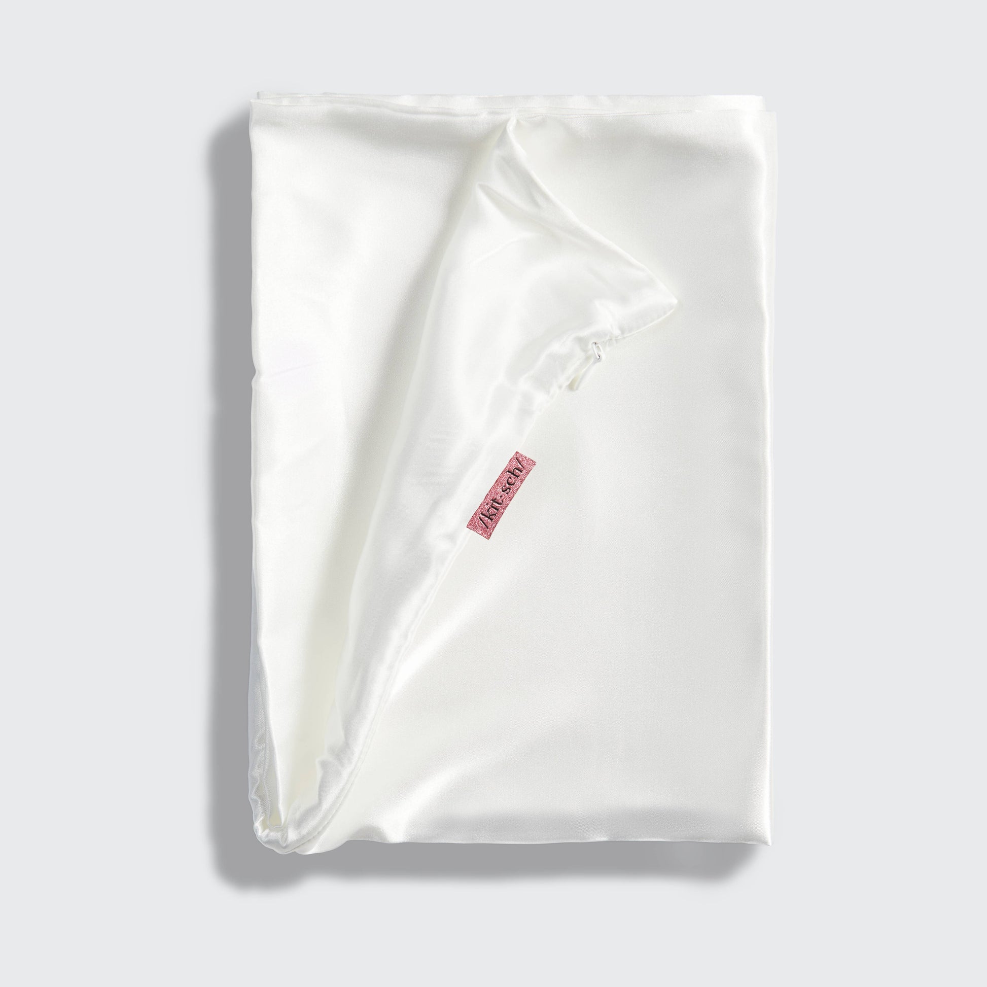 White satin pillowcase with a brand label on a light gray background