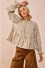 A woman modeling a beige and brown leopard-print long-sleeve blouse with a tie-neck detail, paired with brown wide-leg pants, against a solid beige background.
