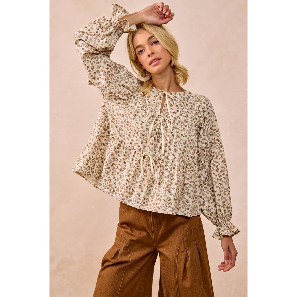 A woman modeling a beige and brown leopard-print long-sleeve blouse with a tie-neck detail, paired with brown wide-leg pants, against a solid beige background.