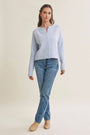 A woman modeling a light blue long-sleeve knit cardigan with a split neckline and button front, paired with blue jeans and beige ankle boots, against a plain cream studio background.