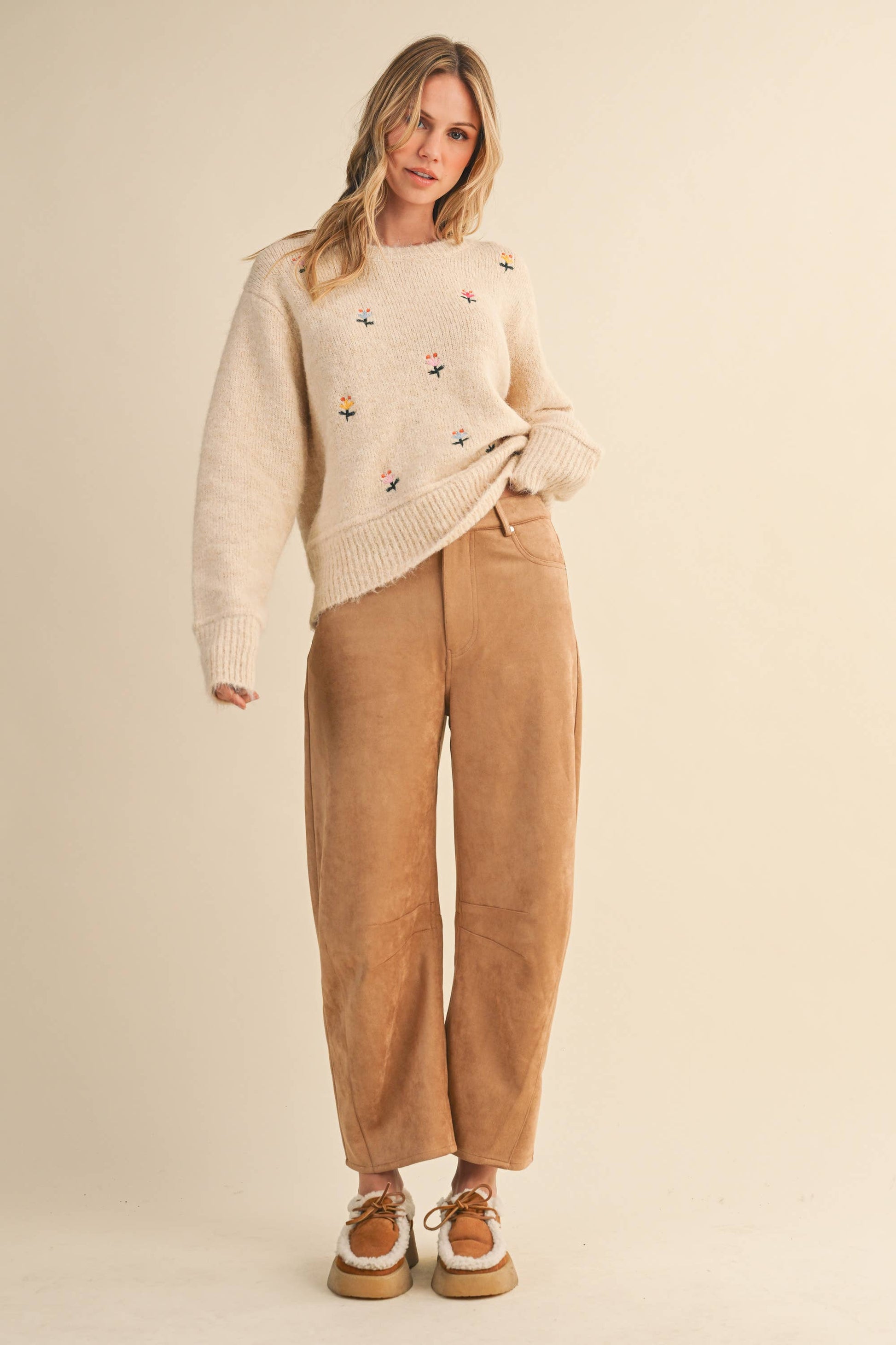 Woman wearing a cream sweater with bird patterns and beige pants on a beige background