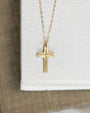 Gold cross necklace on a white card with a wooden surface