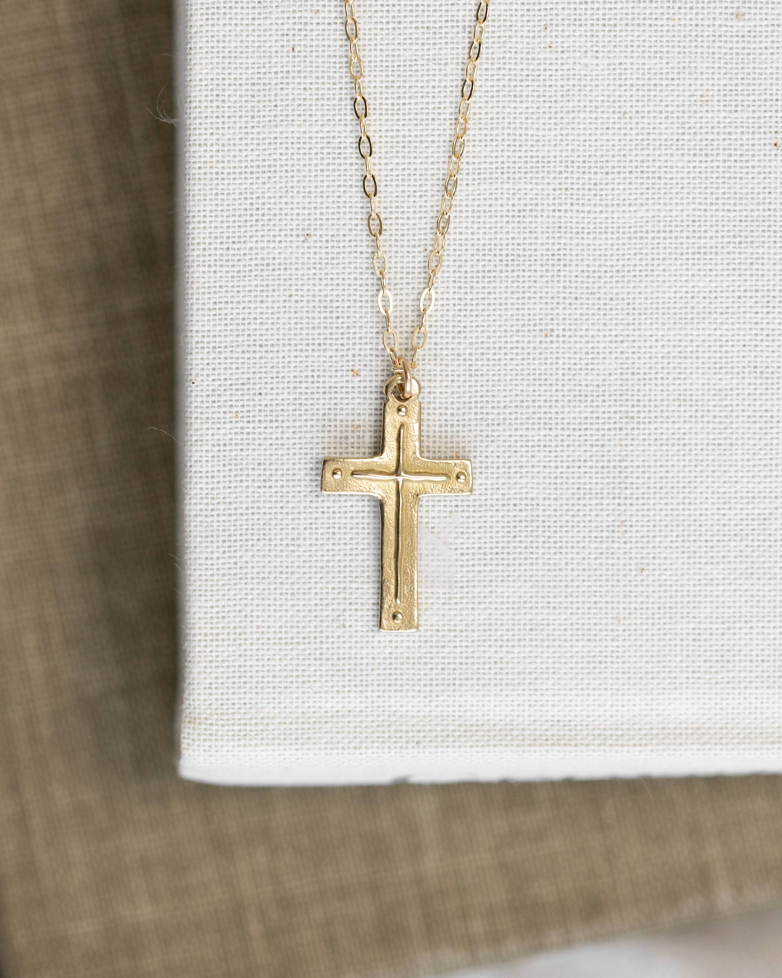Gold cross necklace on a white card with a wooden surface