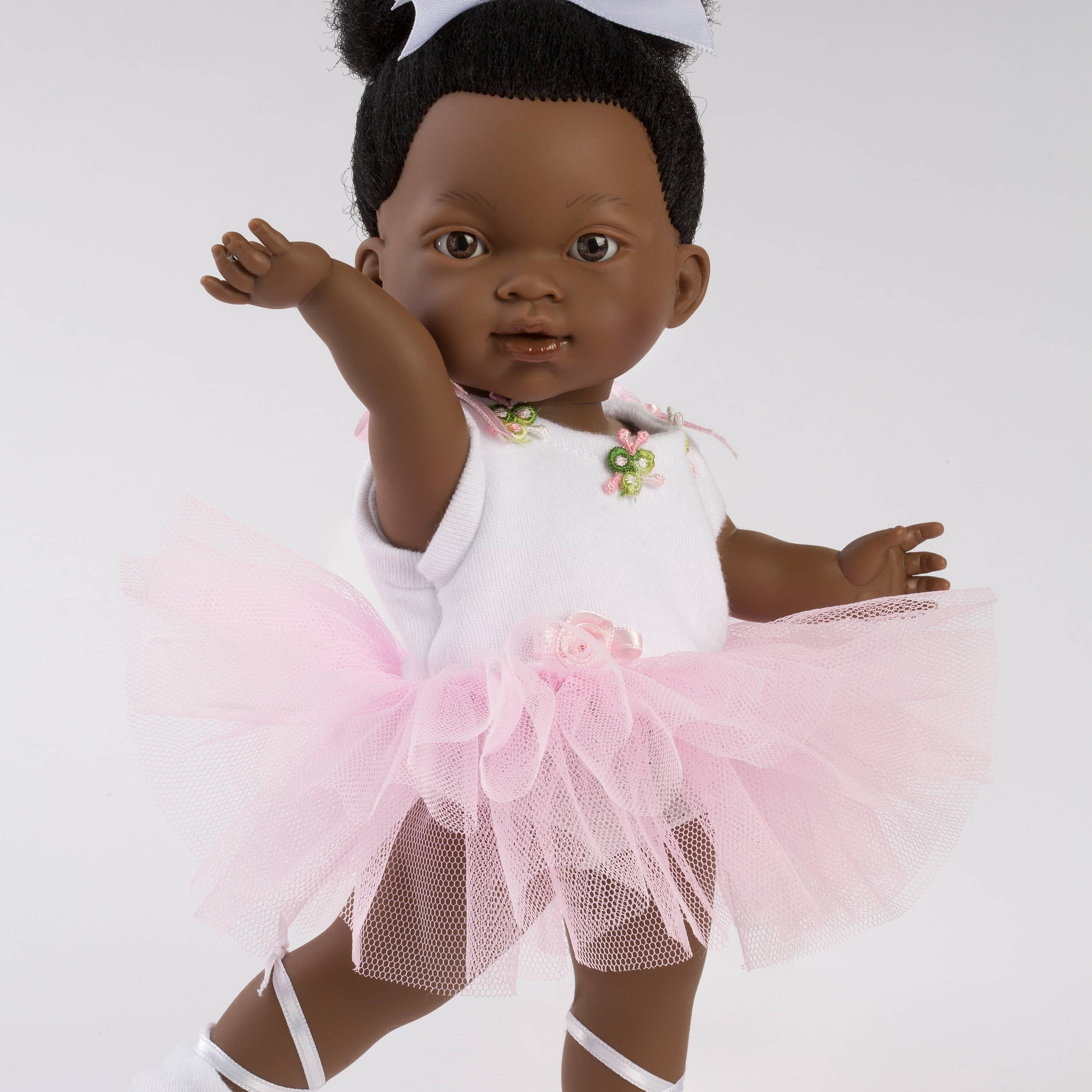 Doll in a ballet outfit with a pink tutu and white shoes on a plain background
