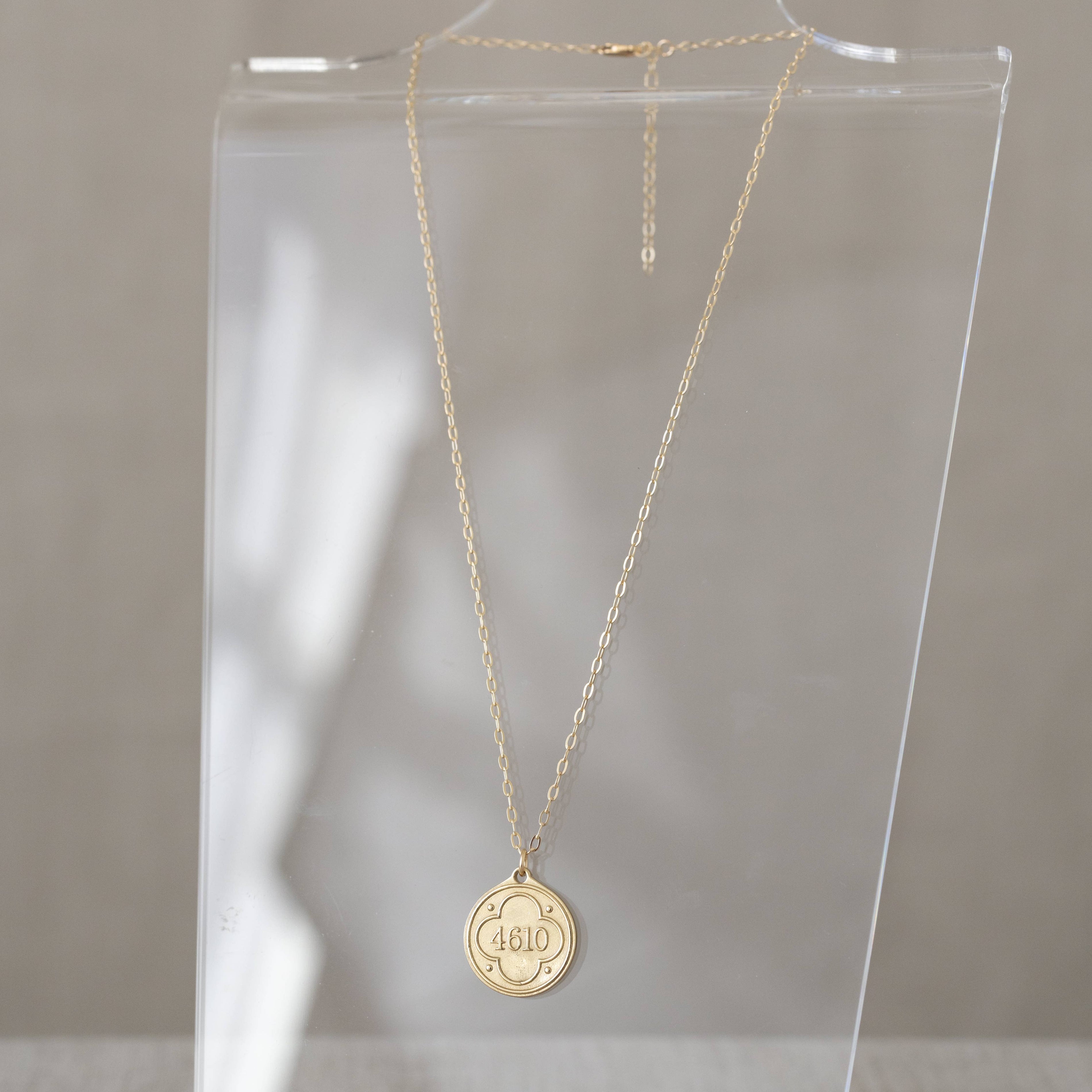 Gold necklace with a round pendant on a clear stand against a neutral background