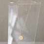 Gold necklace with a round pendant on a clear stand against a neutral background