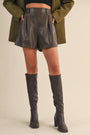 Person wearing dark leather shorts and knee-high boots on a beige background