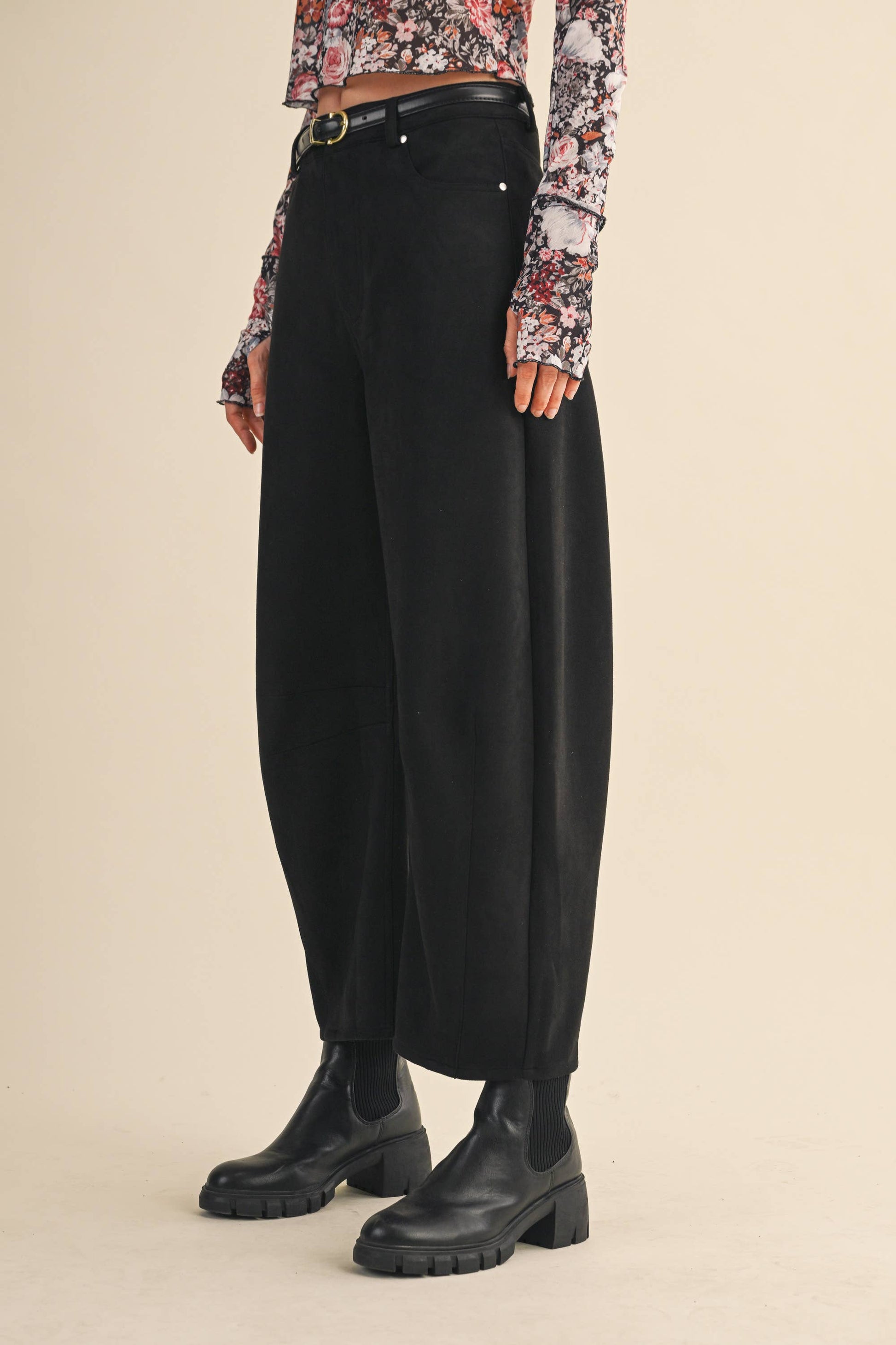 Person wearing black wide-leg pants with a floral blouse on a beige background