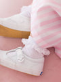 White sneakers with decorative laces worn by a child on a pink background