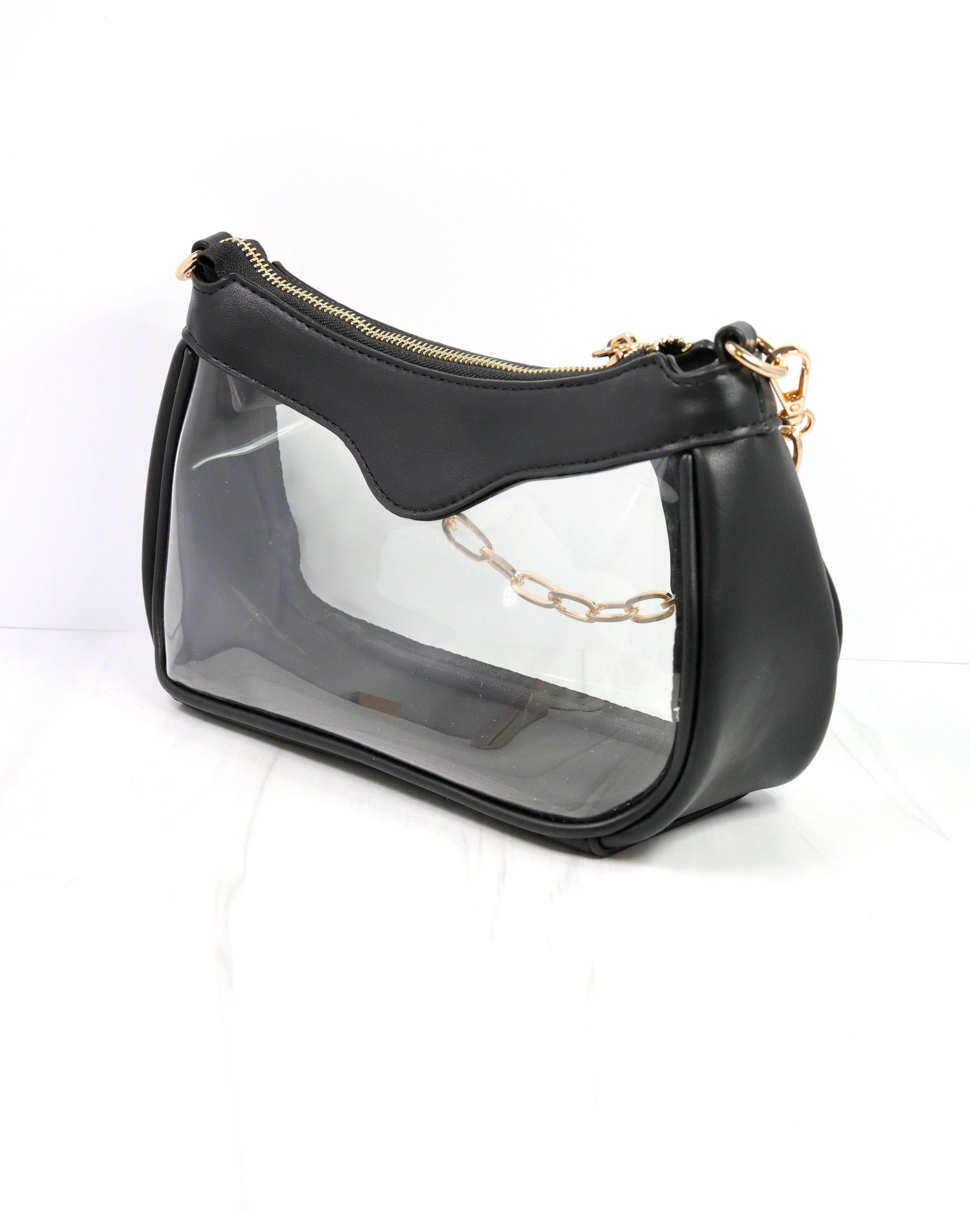 Black handbag with clear front panel and gold chain detail on a white background
