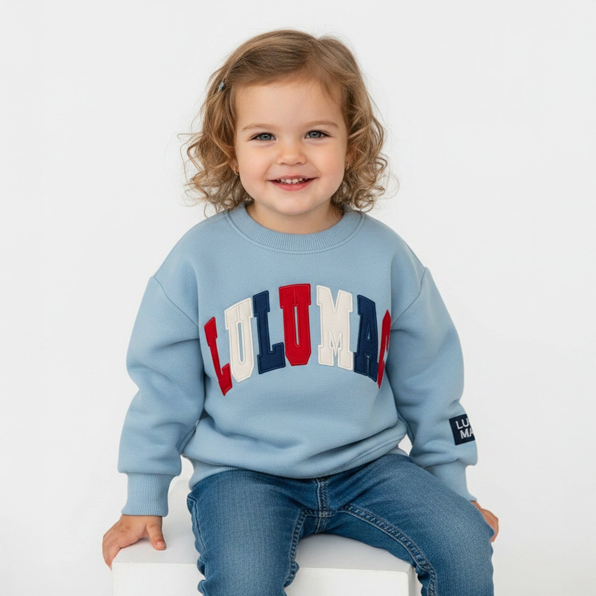 Child wearing a light blue sweatshirt with colorful letters on a white background