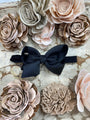 Black hair bow surrounded by beige and pink floral hair accessories on a textured surface