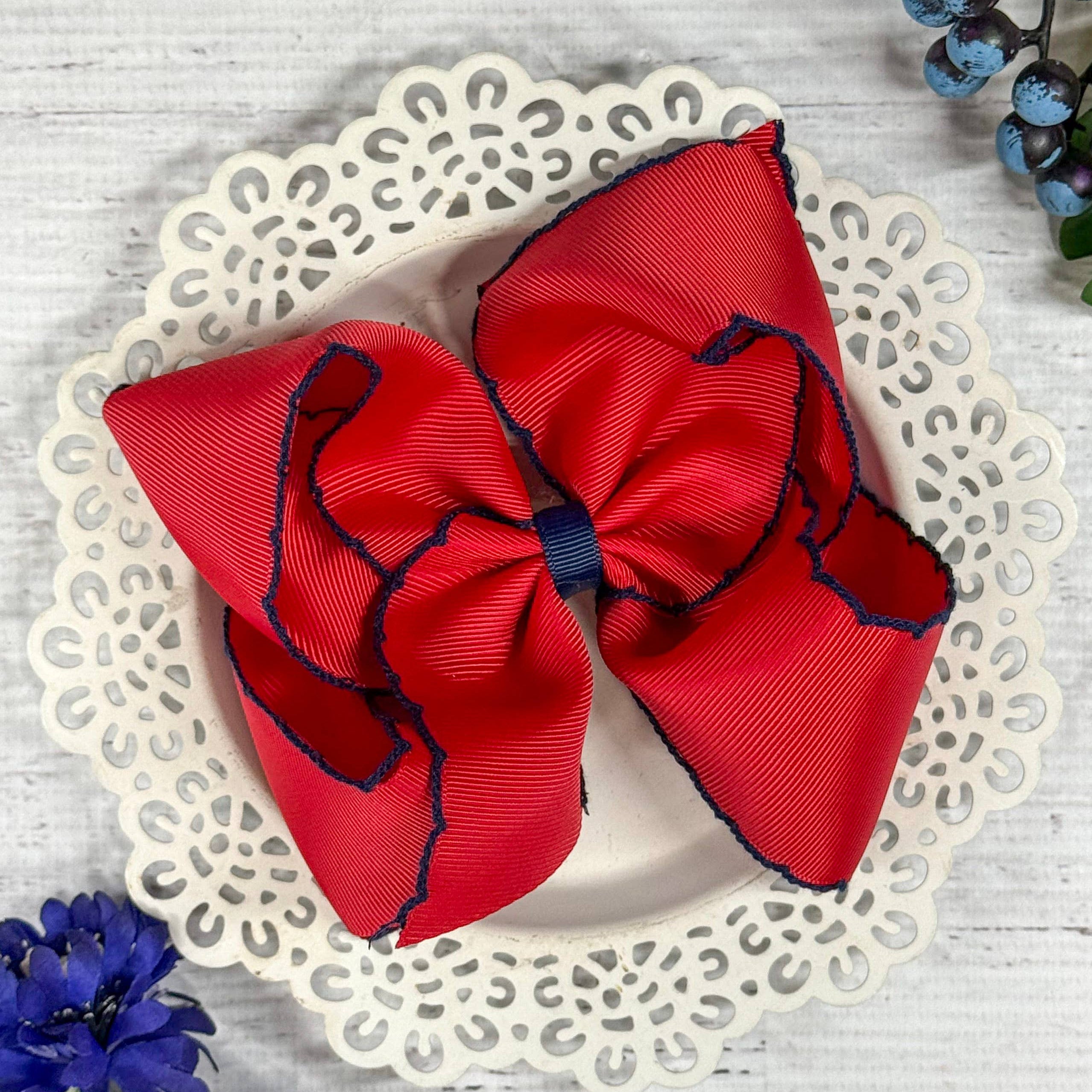 Red hair bow with blue edges on a decorative plate with flowers around.