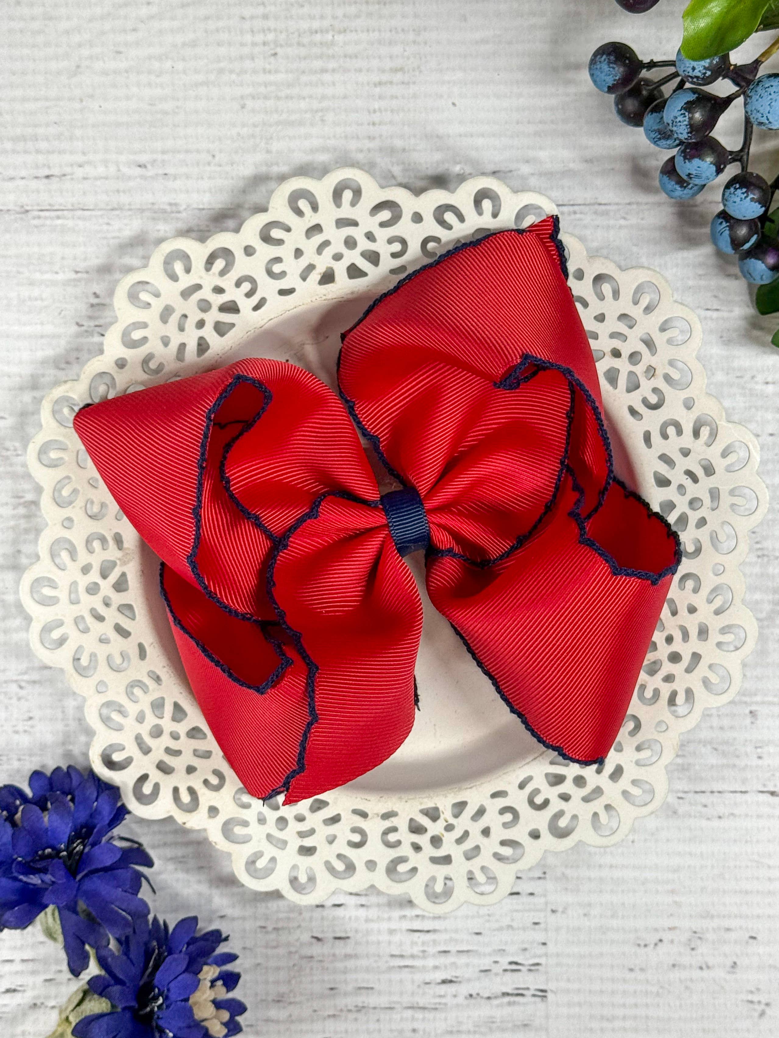 Red hair bow with blue edges on a decorative plate with flowers around.