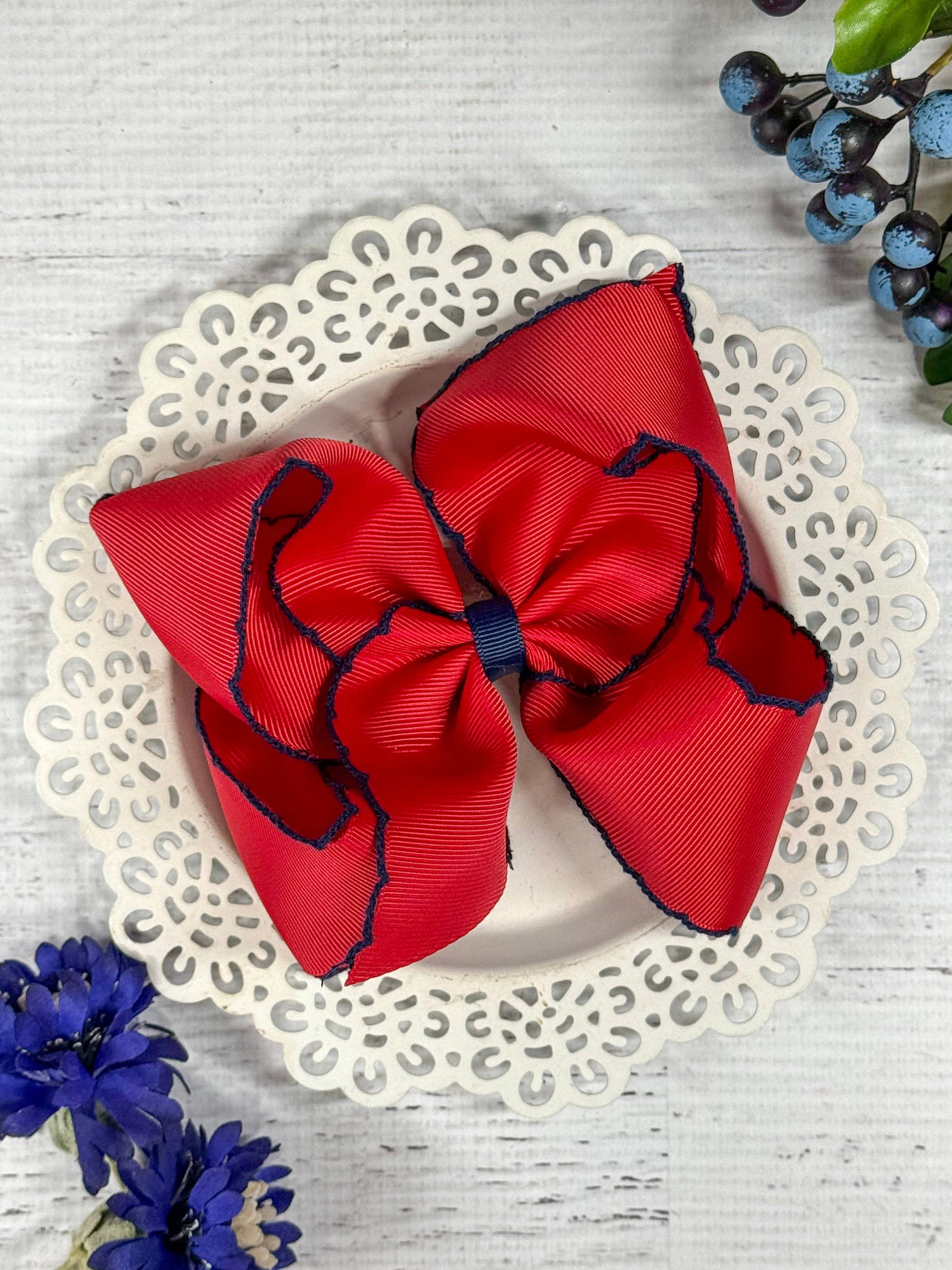Red hair bow with blue edges on a decorative plate with flowers around.