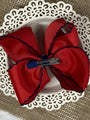 Red bow hair clip with blue edge on a white doily