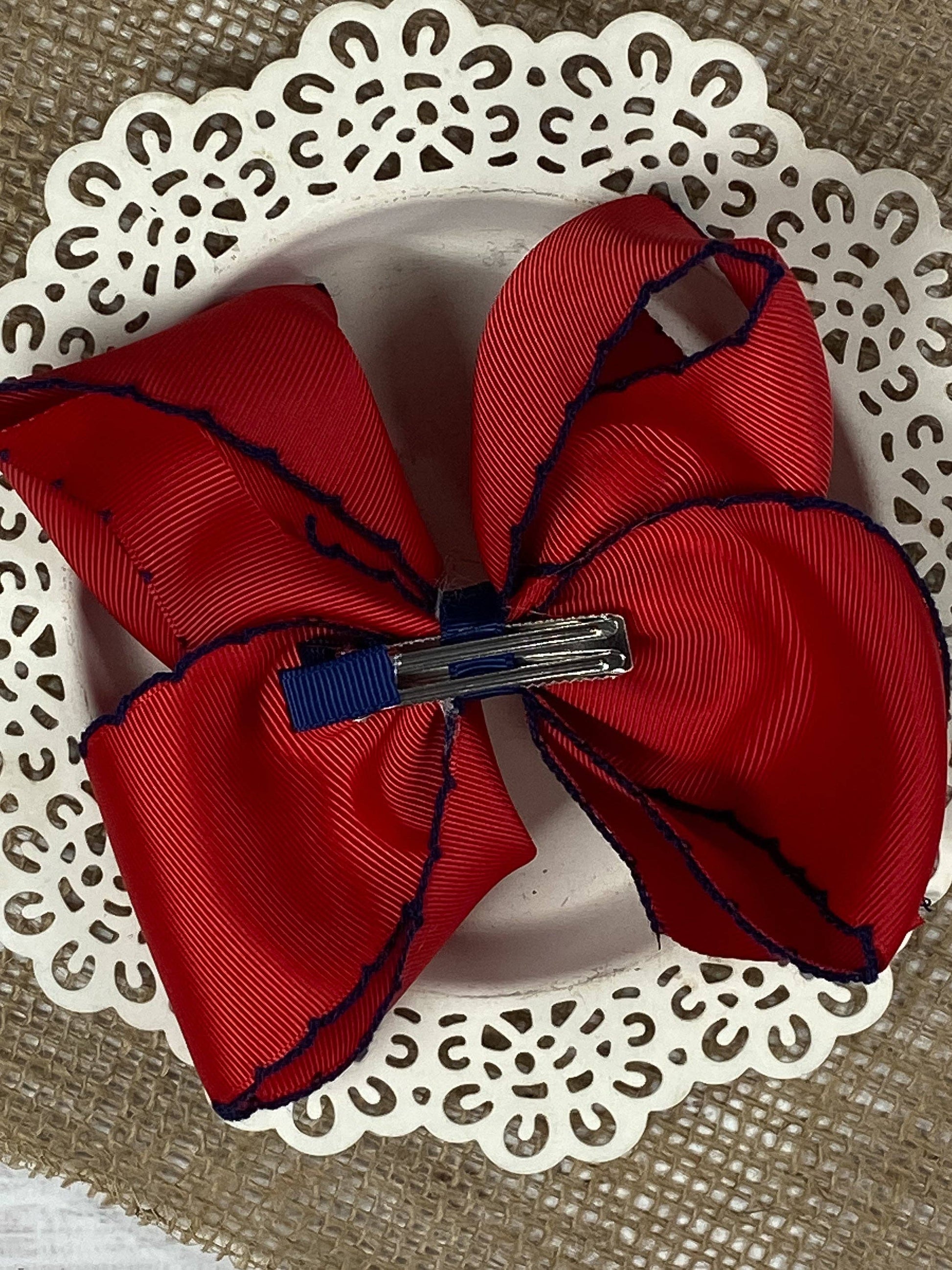Red bow hair clip with blue edge on a white doily