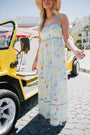 Woman in a patterned dress standing next to a yellow vehicle on a sunny day.