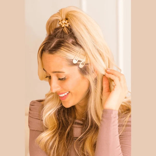 Woman with blonde hair styled in a high ponytail with hair clips, wearing a pink top.