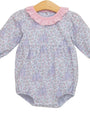 A baby long-sleeve romper with a light purple and pink floral print, featuring a contrasting pink ruffled collar and a smocked waist, displayed on a wooden hanger against a white background.