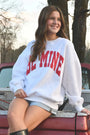 Woman wearing a 'Be Mine' sweatshirt sitting in the bed of a red pickup truck.
