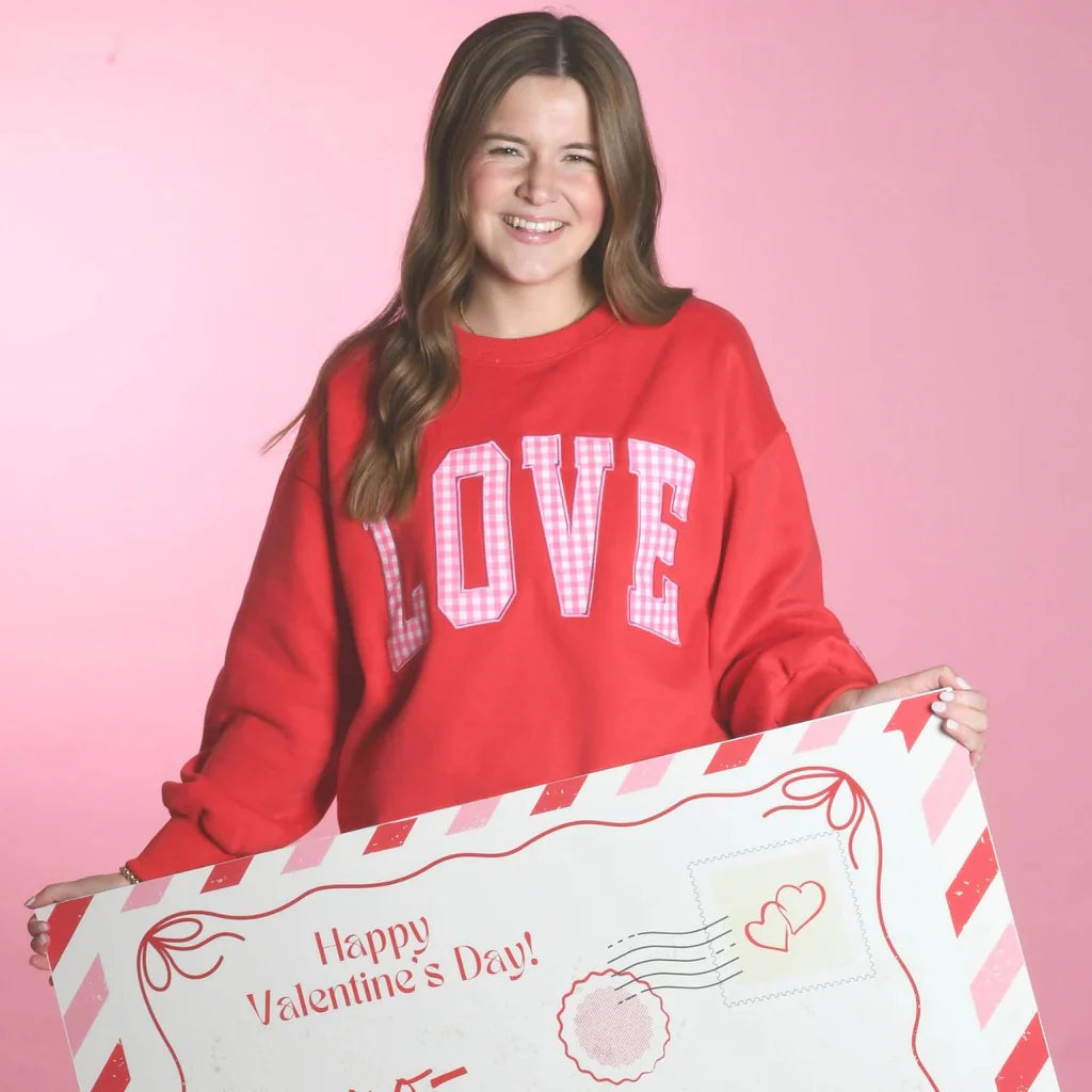 Woman wearing a red sweatshirt with 'LOVE' holding a Valentine's Day card against a pink background