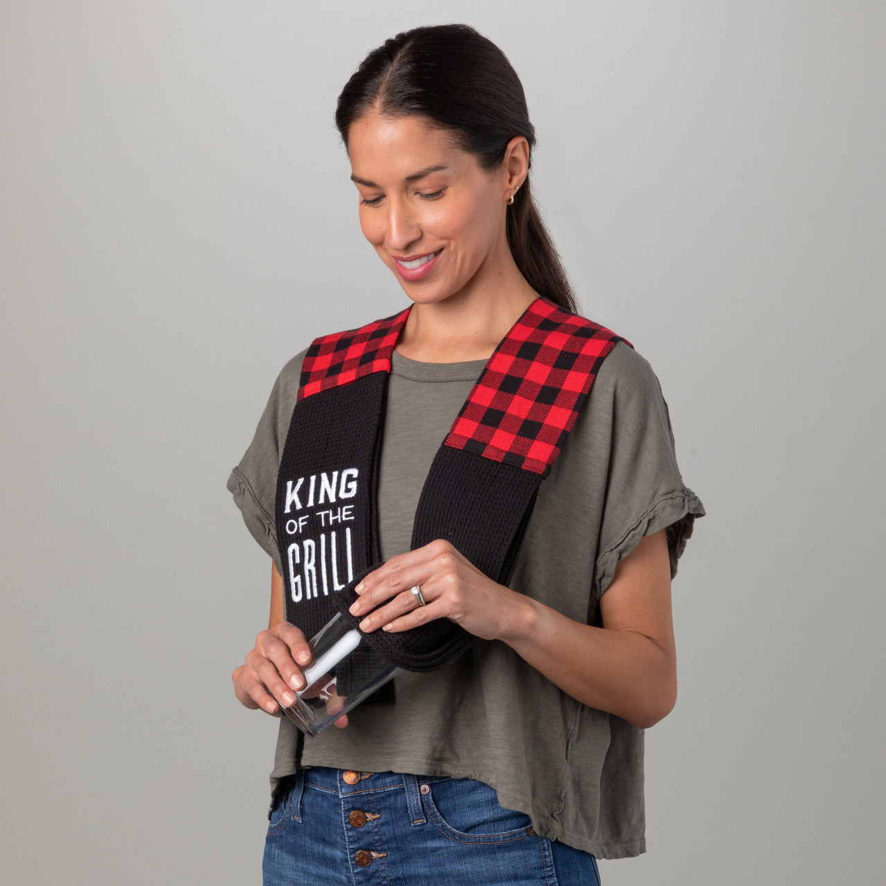 Woman wearing a 'King of the Grill' apron with a red plaid pattern on a gray background