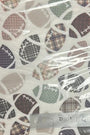 A hand holding a square notebook or notepad with a white cover featuring a pattern of footballs in plaid and solid colors, wrapped in clear plastic on a wooden table.
