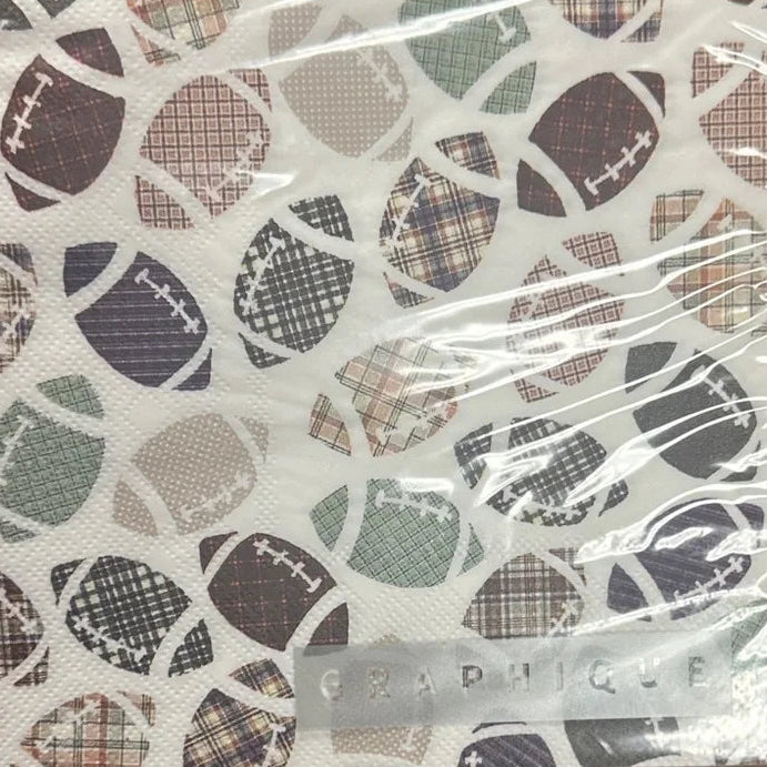 A hand holding a square notebook or notepad with a white cover featuring a pattern of footballs in plaid and solid colors, wrapped in clear plastic on a wooden table.