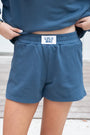 Person wearing blue sweatshirt and shorts with 'LULU MAC' label on a wooden floor.